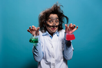 Mad scientist with dirty face and messy hair having beakers filled with liquid substances after...