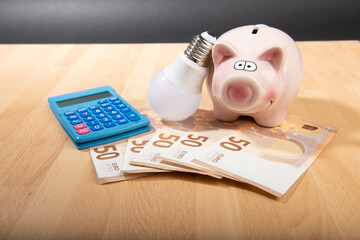 Concept energy price :Piggy bank with light bulb and money on wooden background.