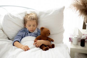 Sweet blond preschool child with teddy bear, lying in bed sick,