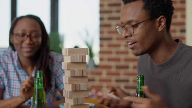 Group of cheerful people having fun with jenga wooden tower, enjoying board games with square blocks and construction pieces. Happy friends playing with cubes for leisure activity.