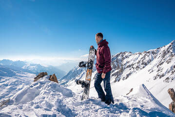 Fototapeta na wymiar Young man holding snowboard while standing on top of snowy mountain on sunny day