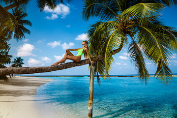 Beautiful woman in a bikini on a palm tree on the paradise beach of Maldives. Sexy model posing in a bikini on the beach. Luxury travels. Holidays on a paradise island. Maldives landscape.