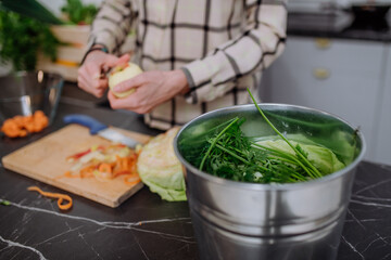 Woman throwing vegetable cuttings in a compost bucket in kitchen.