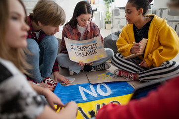 Teenage students sitting at circle in classroom with posters to support Ukraine, no war concept.