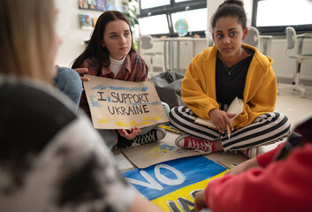 Teenage students sitting at circle in classroom with posters to support Ukraine, no war concept.