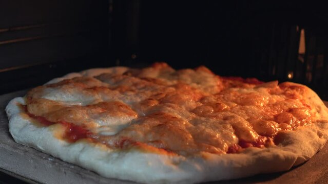 Close up view of cheese on pizza melts from oven heat. Delicious pizza richly strewn with cheese is cooked in the oven. Tasty Italian pizza cheese roasted in the oven on a stone. High quality 4k video