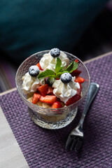 A glass of strawberries with cream, single dessert portion on the edge of restaurant table, side view with copy space