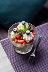 A glass of strawberries with cream, single dessert portion on the edge of restaurant table, side view with copy space