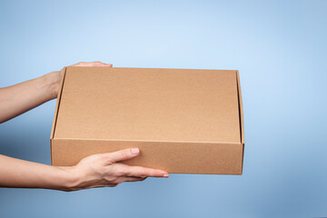 Woman hands holding brown ecological package box made of natural corrugated cardboard. Mockup mailing parcel box on blue background. Packaging, shopping, delivery concept