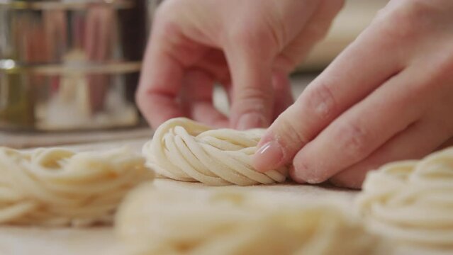 Close up shot of female hands making fresh homemade pasta nests while preparing it for drying or freezing
