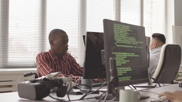 Waist up slowmo of diverse team of software developers typing program codes on their computers while working together in modern open space office