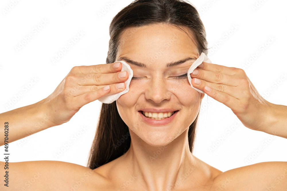 Wall mural a young happy woman removing makeup with the cotton pads on white background