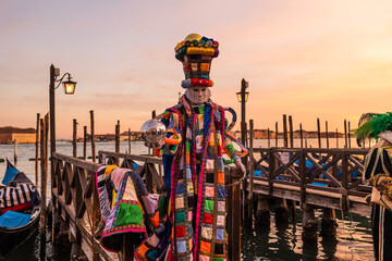 Incredible and colourful sunset in Venice during Venice Carnival - a person in mask and costume is standing by the boats and posing