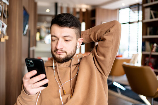 Young man making a video call from his mobile phone. He is sitting in coffee shop. Happy guy enjoying free wireless internet connection at cafe.
