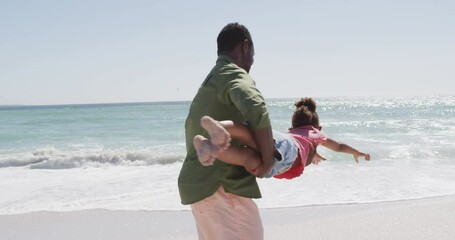 Smiling african american father with daughter playing on sunny beach - Powered by Adobe