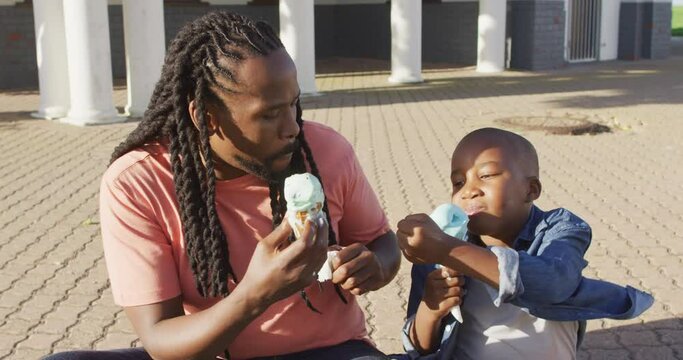 Video of happy african american father and son eating ice creams on sunny day