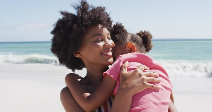 Smiling african american mother with daughter embracing on sunny beach
