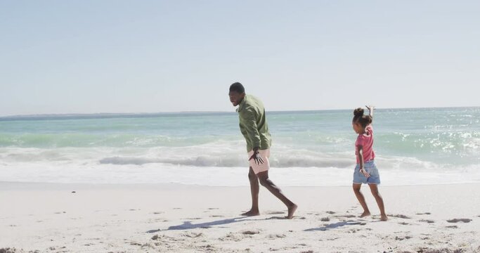 Smiling african american father with daughter playing on sunny beach
