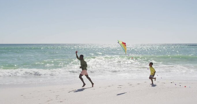 Smiling african american father with son flying kite on sunny beach