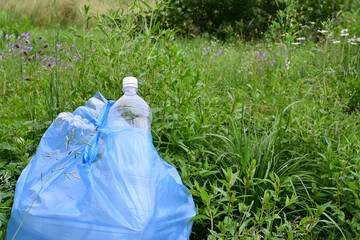 blue garbage bag filled with plastic bottles stands against background of green grass. Close-up. Protection of nature, ecology from pollution. World Environment Day, concept of Earth Day
