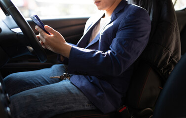 Man sitting in car using mobile phone to text while driving. Close-up of businessman while driving typing message on mobile phone.