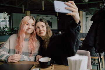 Cheerful young lesbian couple selfie using mobile phone at a coffee shop. Two joyful attractive Asian girls together at restaurant or cafe.