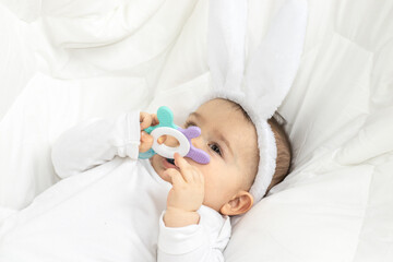 Obraz na płótnie Canvas super cute little baby toddler infant boy with bunny ears on head and teething toy in hand. adorable child on white blanket smiling and chewing the toy. easter bunny holiday concept. year of rabbit 
