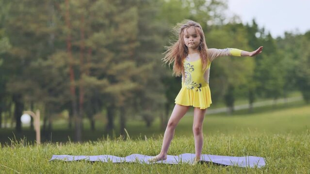 A little girl performs the elements of rhythmic gymnastics in the park.