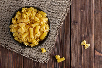 Different kinds of raw pasta in bowl on wooden background.