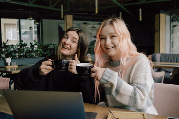 two happy young women sitting in coffee shop looking at laptop computer