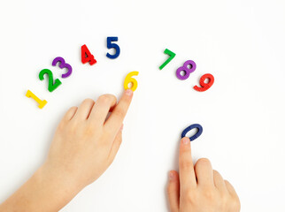 Children's hands move numbers on a white table. Learning colors and to count from zero to ten