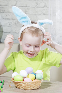 Easter kids. Happy boy in rabbit ears on his head plays with colored eggs at home. Preparing for Easters the Big Egg Hunt. Easter Bunny. Easter eggs. Vertical photo