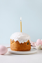 Easter cake with burning candle and pink eggs on blue background. Celebration religion custom. Vertical format.