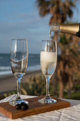 Pouring of Spanish cava sparkling wine is glasses with view on blue sea and sandy beach, Costa del Sol vacation destination, Andalusia, Spain