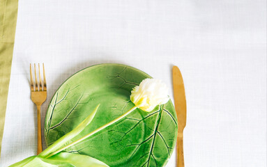 Table setting. Green plate with a flower. Knife and fork.
