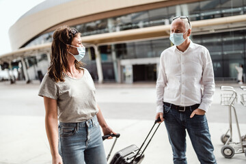Travellers in protective masks chatting while leaving the airport with their luggage