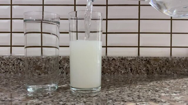 Man pouring water into the raki glass and bleaching it close up view
