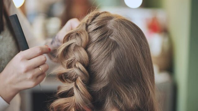 The girl makeup artist makes a braid for the model.