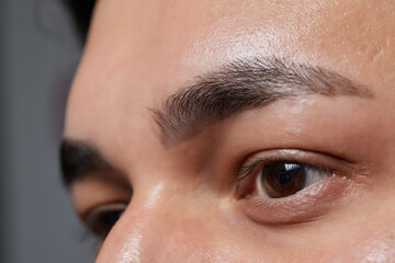 Professional barber doing threading procedure and correcting shape of eyebrows to young male client...