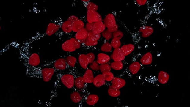 Super slow motion shot of rotating exploded raspberries with splashing water on black at 1000fps.