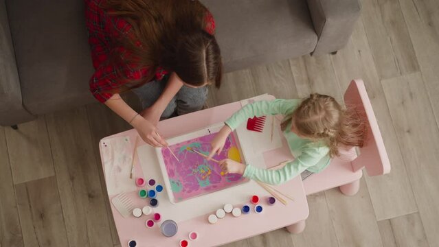 Woman and girl add bright colors to pattern on oily water