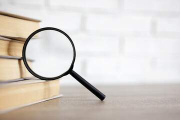 education and research concept - stack of books and magnifying glass on the table in library, copy space over white background - Powered by Adobe