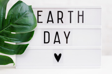 Earth day concept - lightbox with earth day words and green leaf of monstera plant