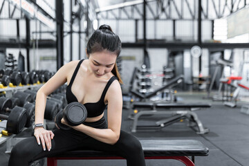 Fototapeta na wymiar exercise concept The working out lady paying attention on carrying a dumbbell with her right hand while sitting on the bench earnestly