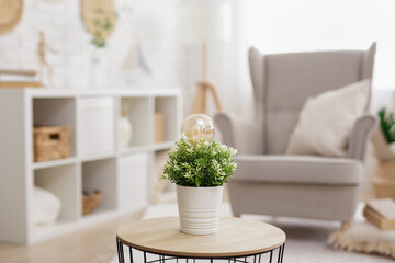 green energy concept - close up of light bulb in green potted houseplant in modern interior
