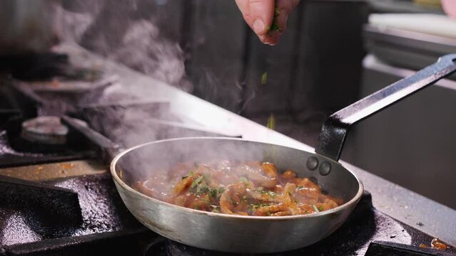 Making fried pork Brasso style - adding herbs to the meat in a pan, tossing and mixing