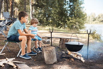 Children sitting around a campfire in forest in summer. Family picnic outdoors. Camping life....
