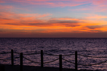 Naklejka na ściany i meble Rope bridge silhouette at sunset. Beautiful seascape, bright orange sky and sea