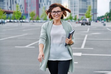 Smiling successful mature business woman walking outdoor, modern urban style background.