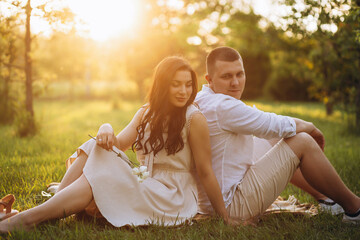 A romantic couple is relaxing while sitting on the grass and looking at faces of each other.